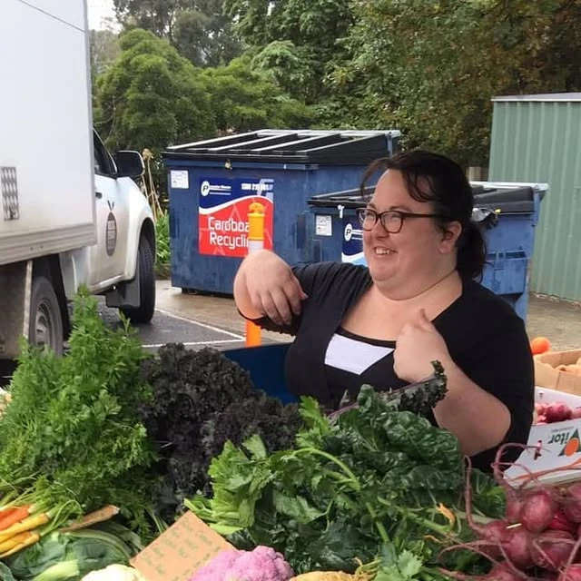 Janelle behind a display of fresh vegetables at Real Food Grocer